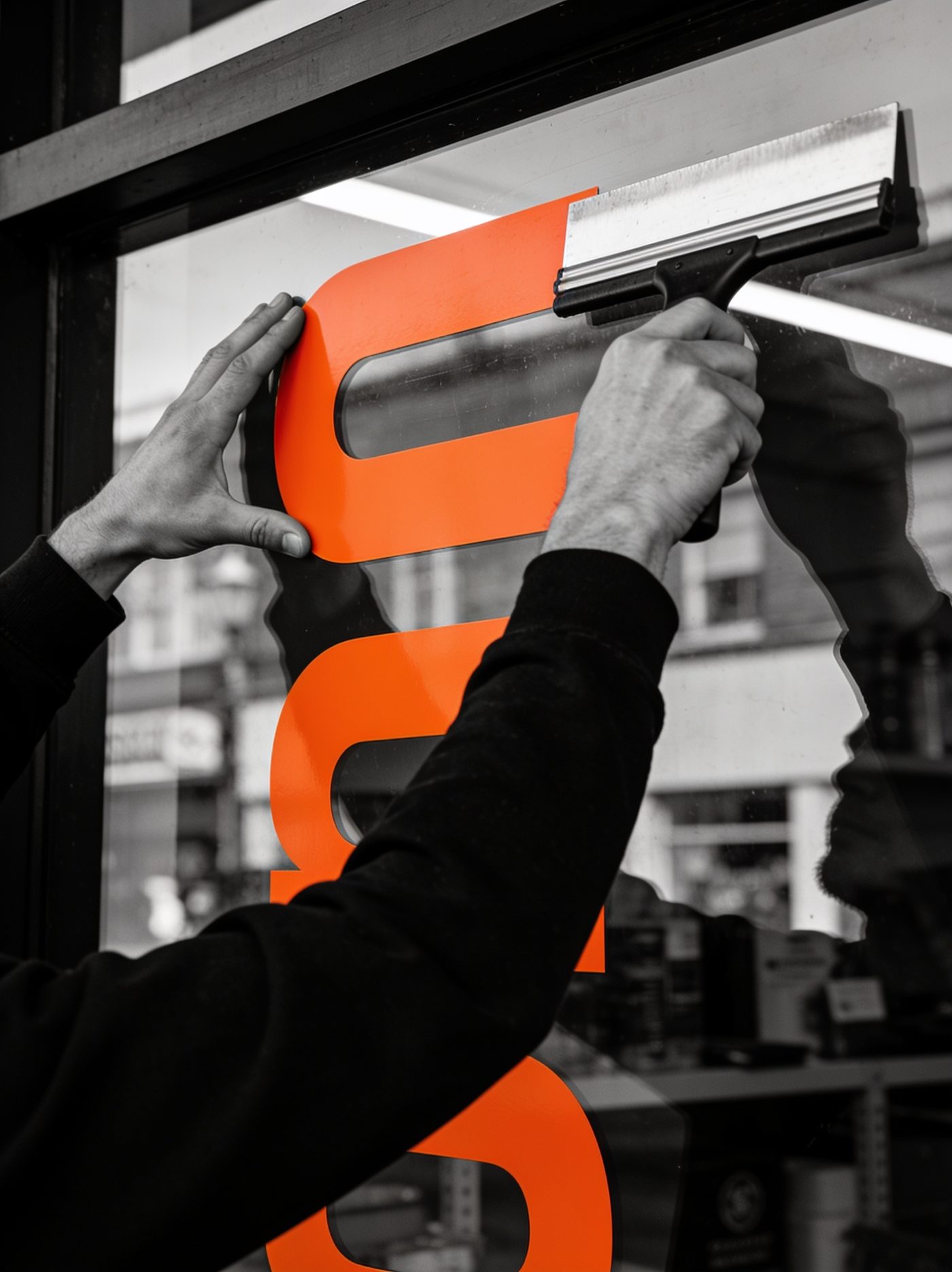 Orangefarbene Folie wird mit Rakel auf Schaufenster aufgezogen
